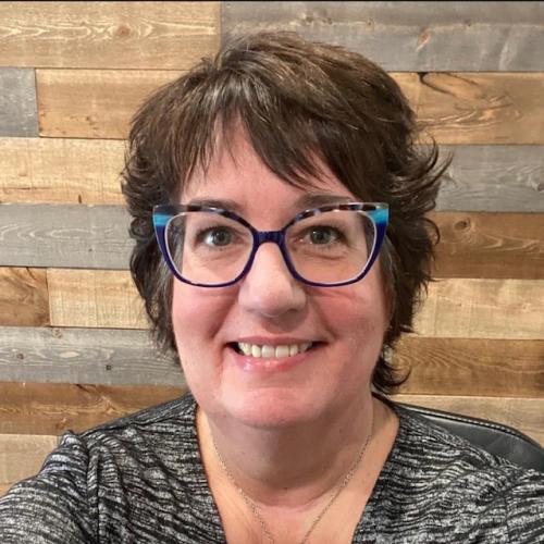 Debbie smiling in front of wood panel wall